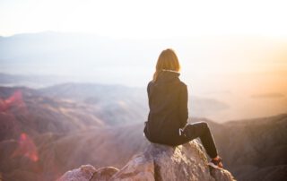 Junge Frau sitzt allein auf einem Berggipfel